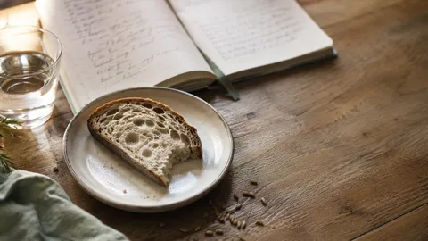 Tranche de pain au levain sur une table en bois, à côté d'un carnet ouvert, lumière naturelle douce