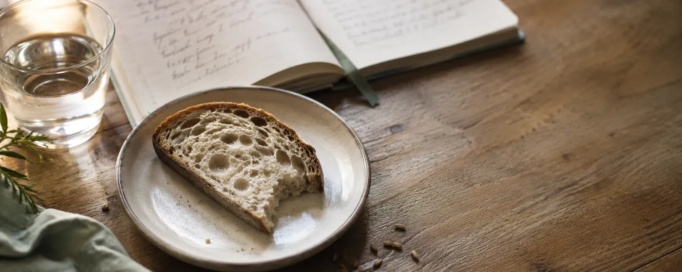 Tranche de pain au levain sur une table en bois, à côté d'un carnet ouvert, lumière naturelle douce