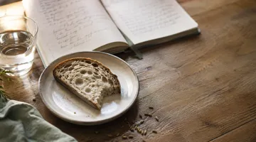 Tranche de pain au levain sur une table en bois, à côté d'un carnet ouvert, lumière naturelle douce